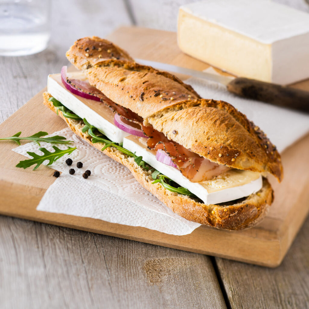 photo culinaire, du fromage Le Brie dans un sandwich de pain aux céréales, sur une planche en bois.