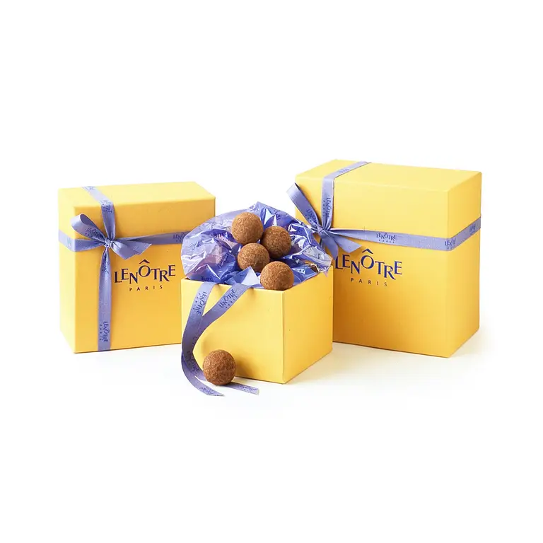 Coffret avec un trio de  boîtes jaunes Lenôtre et ruban violet, truffes en chocolat visibles dans la boîte ouverte — Présentation luxe, pour un chocolatier.