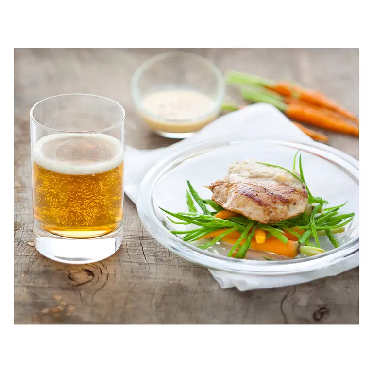 Verre de cidre doré servi avec escalope grillée posée sur julienne d’haricots verts et carottes avec une assiette transparente sur bois rustique, dans un décor de studio photo professionnel.