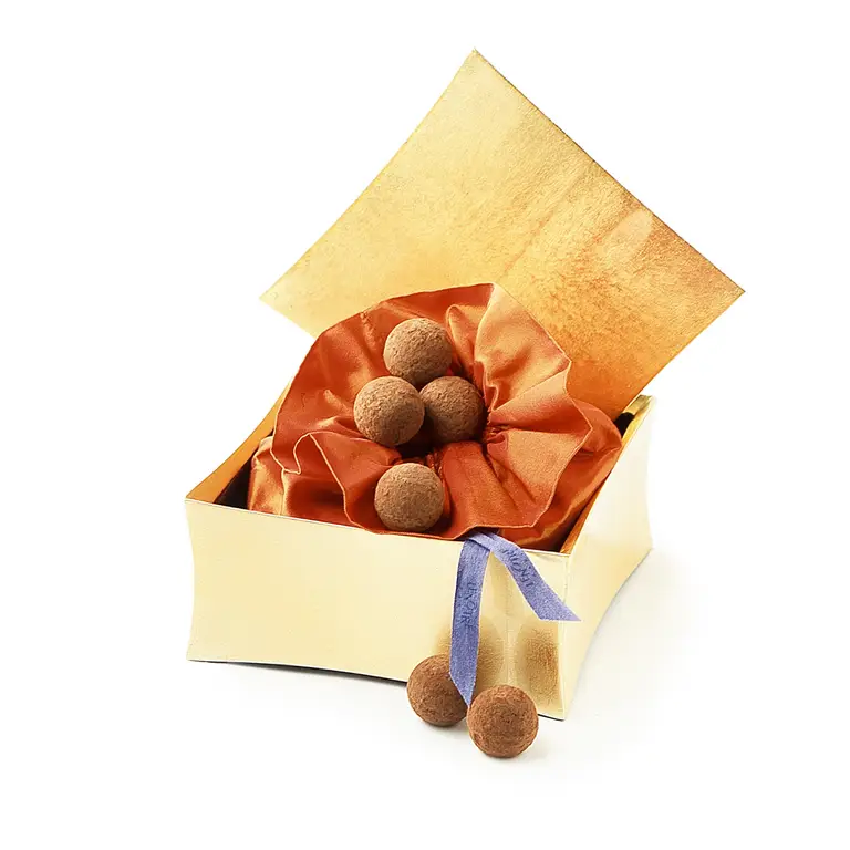 Coffret cadeau doré garni de truffes au chocolat poudrées, posé sur satin cuivré avec ruban violet — packshot studio photo.
