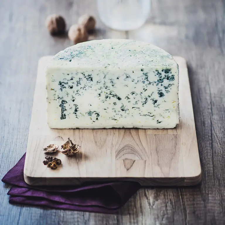 Demi-meule d’un fromage bleu crémeux,  persillé, présenté sur une planche en bois, avec des morceaux de noix pour une promotion des fromages persillés.