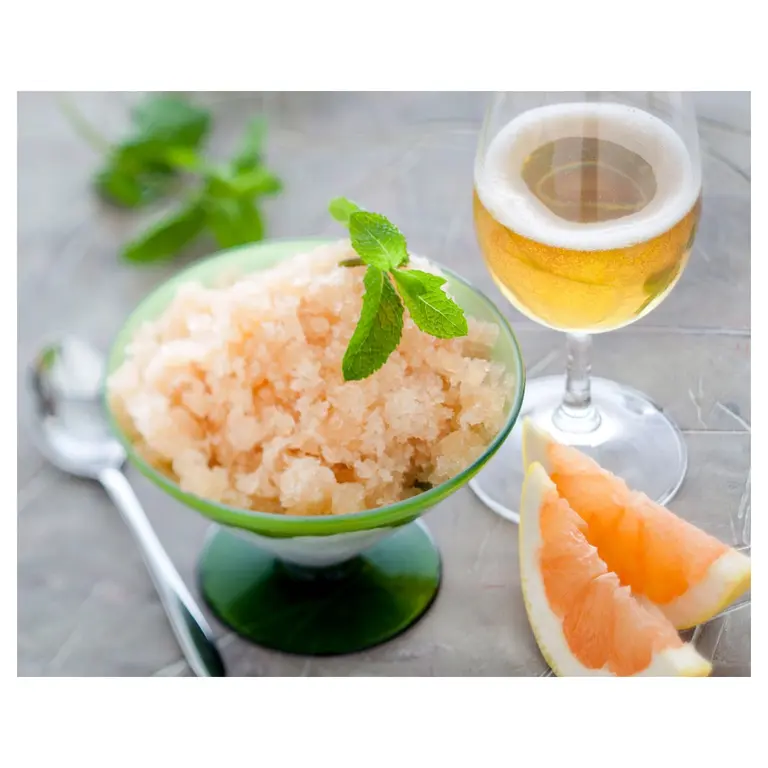 Granité au pamplemousse rose garni de feuilles de menthe, servi en coupe verte, avec verre de cidre et quartiers de pamplemousse sur fond clair, photo culinaire en lumière naturelle.