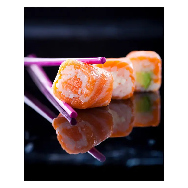 Rangée de makis au saumon sur une surface miroir noire, baguettes violettes en diagonale — jeu de reflets dynamique, pour présentation d’une carte menu d’un restaurant japonais.