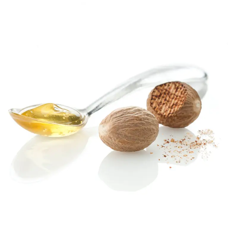 Cuillère de miel, noix de muscade entières et râpée sur un blanc très épuré, pour une présentation en hero shot.