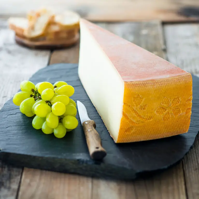 Morceau de fromage, croûte lavée, raisins verts sur une ardoise avec un couteau, lumière 3/4 contre jour pour une présentation d’un artisan fromager.