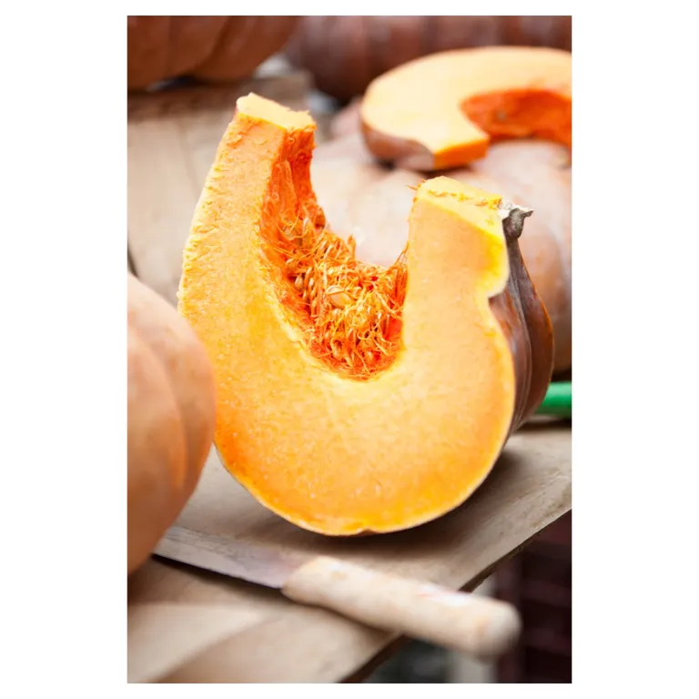 Quart de potiron frais coupé, pulpe orange et graines apparentes, posé sur planche en bois avec couteau ; autres courges floutées en arrière-plan, lumière naturelle—photographie culinaire professionnelle pour fiche produit / marché.
