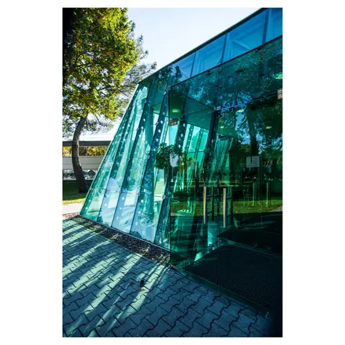 photographie d’architecture, d’une perspective extérieure d’un volume en verre aux trames inclinées, reflets des arbres et entrée intégrée dans le plan de façade.