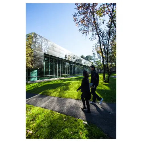 photographie corporate, avec une vue d’ensemble avec deux usagers en mouvement longeant une façade toute hauteur, pelouse et arbres en premier plan.