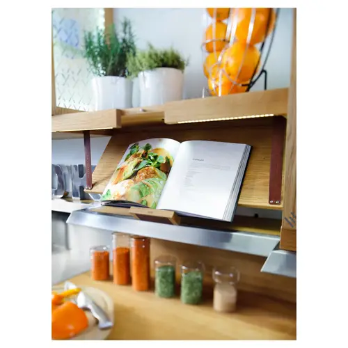 Détail de cuisine aménagée avec livre de recettes ouvert, bocaux d’épices et herbes en pot.