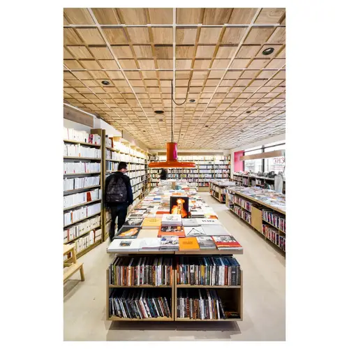Vue d’ensemble d’une librairie contemporaine, plafond bois quadrillé, tables de nouveautés — reportage de photographie d’architecture à Paris.