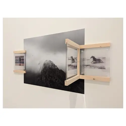 Gros plan sur un montage mural : grand tirage noir et blanc de paysage montagneux entouré de deux petits cadres vitrines en bois clair, intégration scénographique en relief.