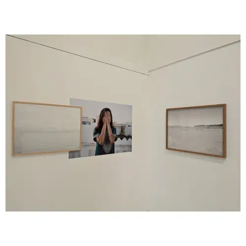 Angle de salle avec un portrait couleur au centre et deux paysages encadrés de part et d’autre, accrochage épuré sur murs blancs.