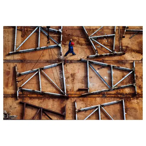 Vue aérienne d'ouvrier en casque rouge marchant sur structure métallique rouillé avec cables de levage, chantier naval