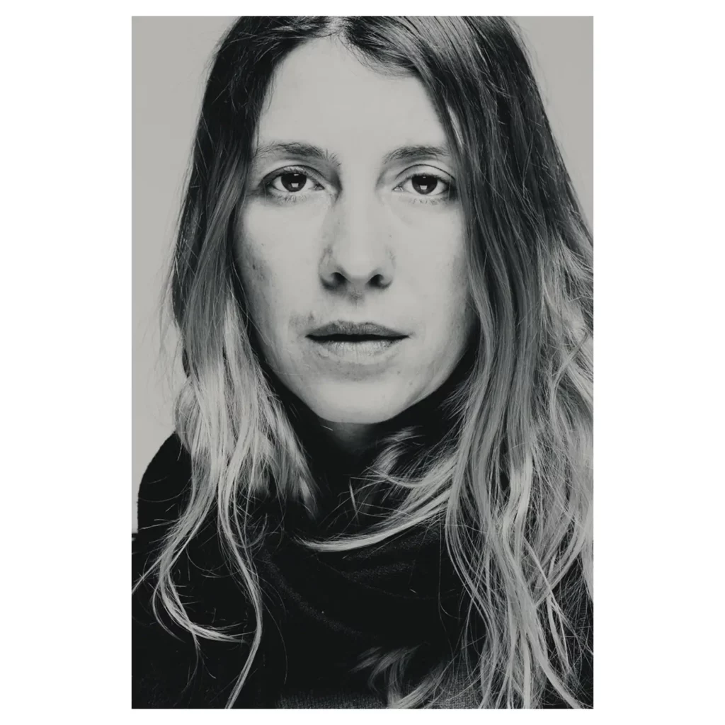 Portrait noir et blanc d’une femme aux cheveux ondulés, cadrage serré, regard caméra, lumière douce, écharpe sombre, fond studio — style éditorial.