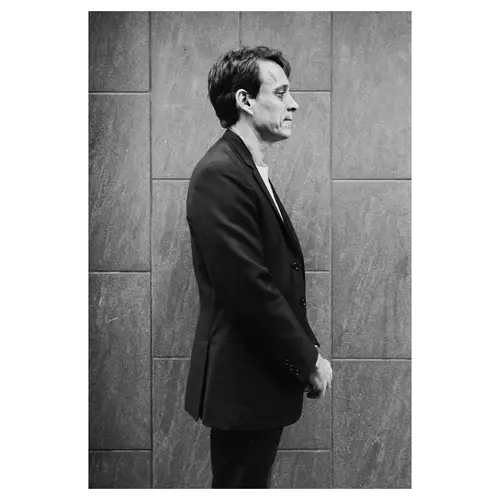 Portrait profil d’un architecte devant un parement minéral — prise de vue corporate en noir et blanc.