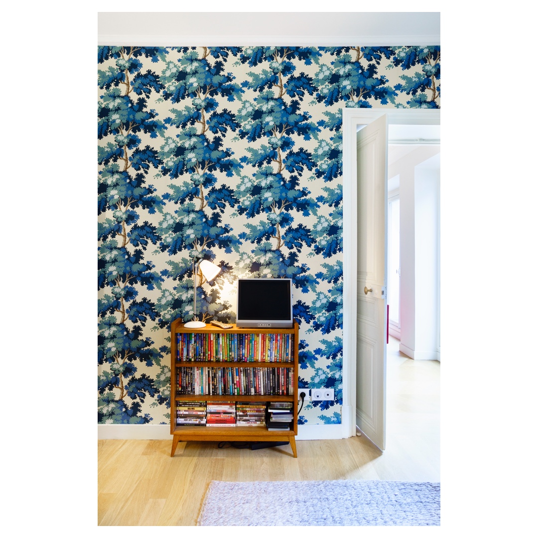 Papier peint feuillage bleu, meuble bas vintage avec livres/écran, porte ouverte — reportage photo déco d’appartement à Paris.