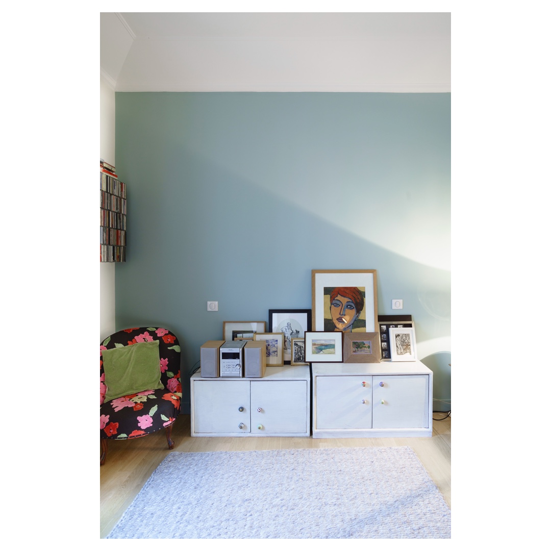 Mur vert d’eau, meubles blancs et cadres posés, fauteuil fleuri — photographe d’architecture intérieure à Paris.