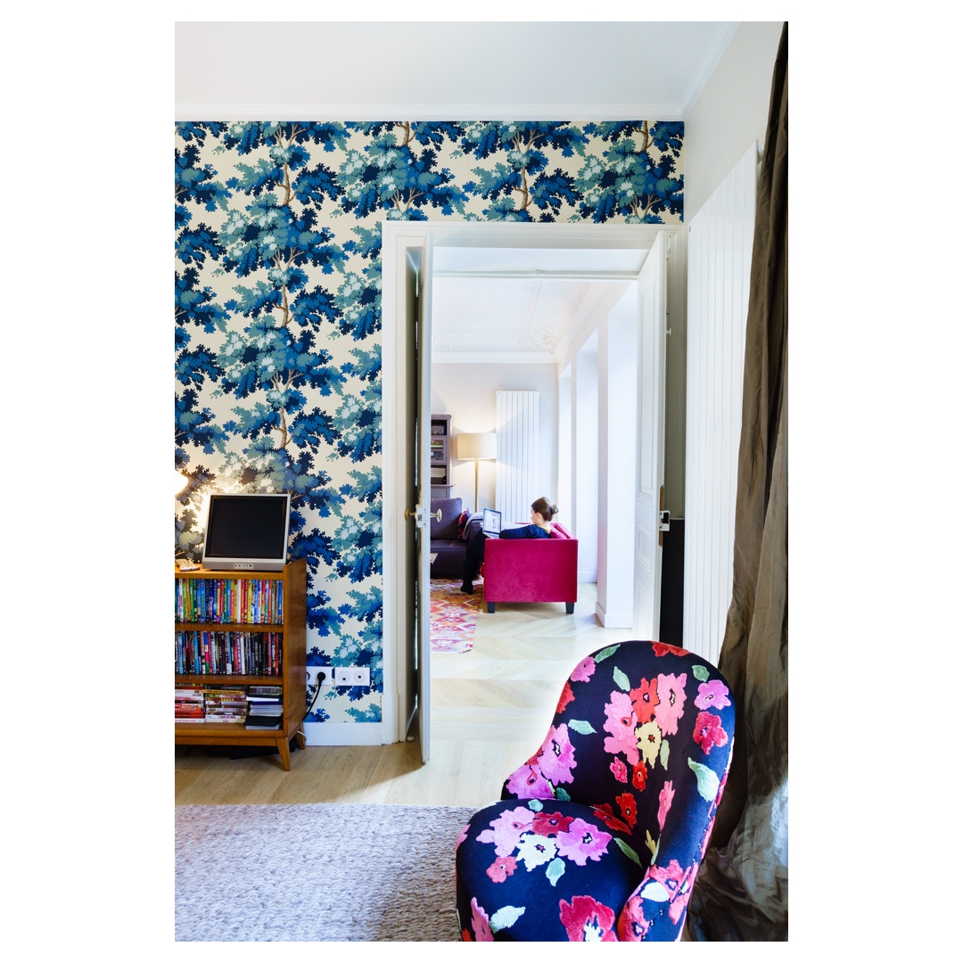 Vue en enfilade : papier peint bleu, double portes vers salon, fauteuil fleuri — reportage photo architecture à Paris.
