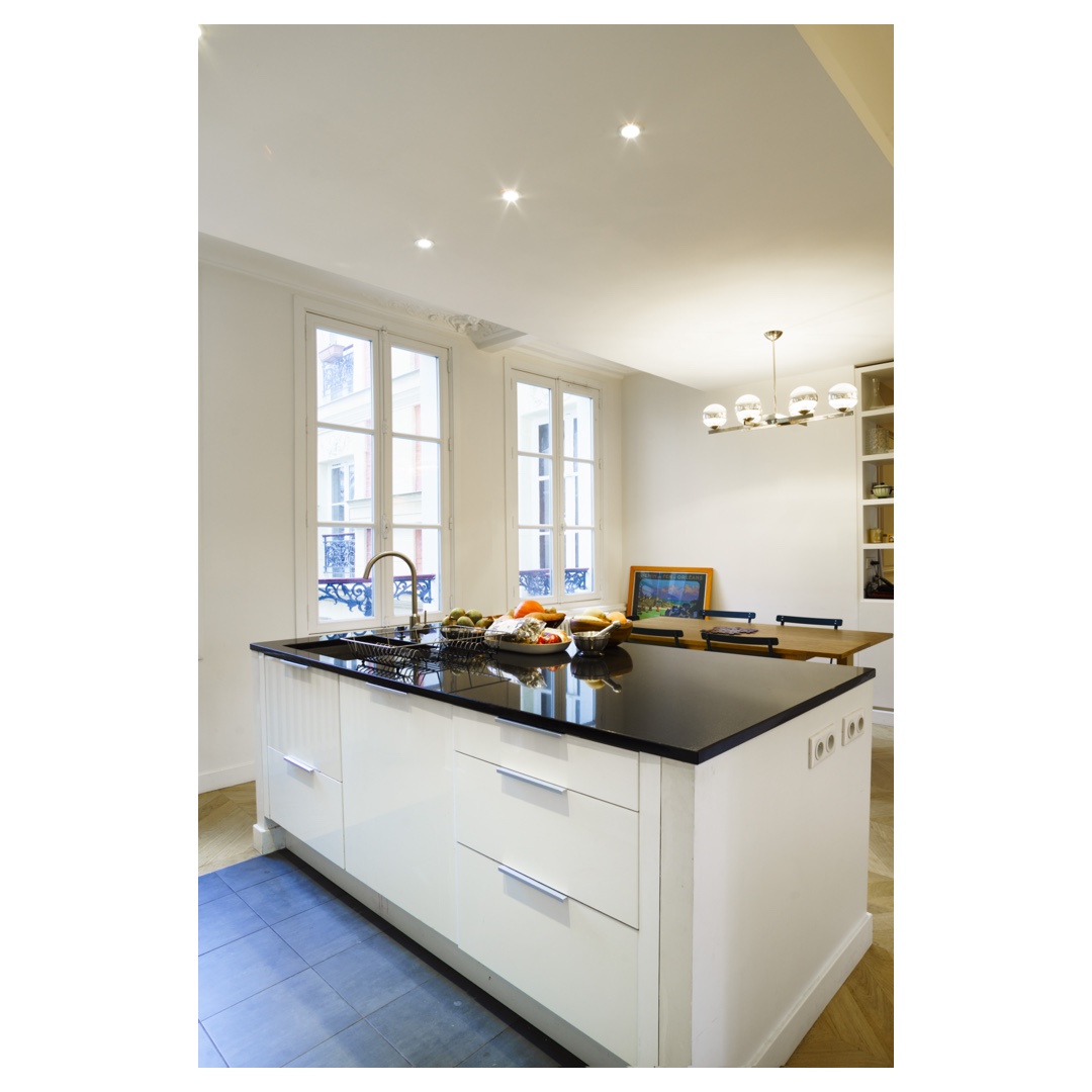 Cuisine parisienne avec îlot blanc laqué et plan noir, lumière naturelle — photographie d’architecture intérieure.
