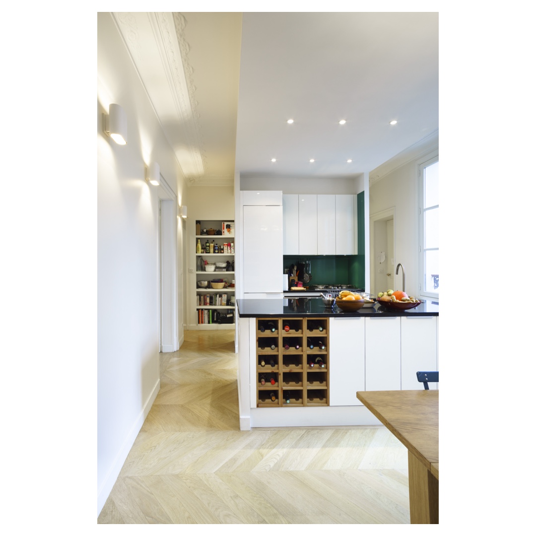 Cuisine avec îlot et range-bouteilles, crédence verre vert, parquet pointe de Hongrie — architecture intérieure Paris.