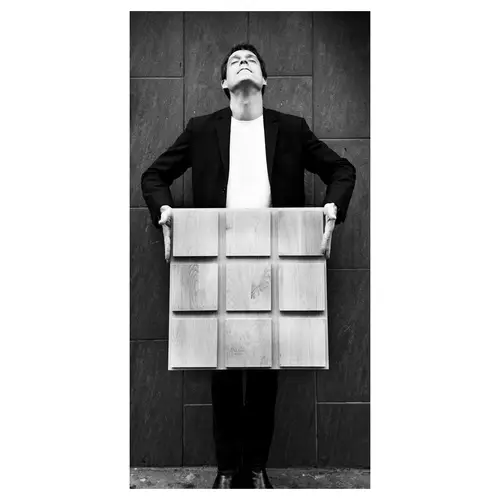 Portrait en pied d’un architecte tenant un module de plafond bois — photo N&B pour projet d’aménagement intérieur.