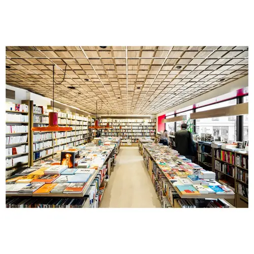Allée centrale de librairie, tables thématiques, éclairage suspendu rouge et plafond bois — photo d’architecture intérieure à Paris.
