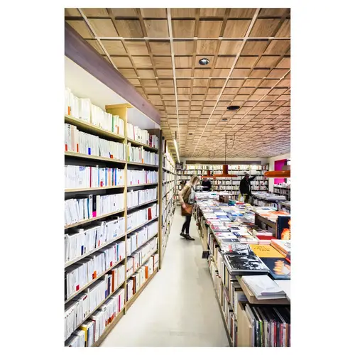 Perspective d’allée entre rayonnages, circulation clients, plafond bois modulaire — reportage architecture commerce.