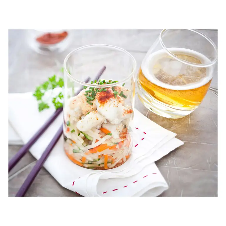 Verrine de salade de poisson blanc aux légumes croquants, ciboulette et paprika, accompagnée d’un verre de cidre sur une nappe claire, pour la promotion de la filière cidre.