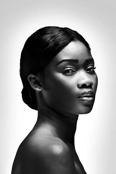 Portrait femme en noir et blanc, profil trois quarts, cheveux attachés, lumière studio sur fond blanc, photo portrait réalisée à Bordeaux.