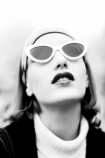 Portrait noir et blanc en contre-plongée d’une femme avec lunettes œil-de-chat et bandeau, look mode vintage — photographe portrait à Bordeaux.
