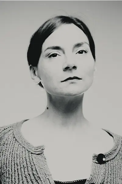 Portrait studio noir et blanc d’une femme, regard légèrement vers le haut, cheveux attachés, cardigan en maille, fond gris clair — photographe portrait à Bordeaux