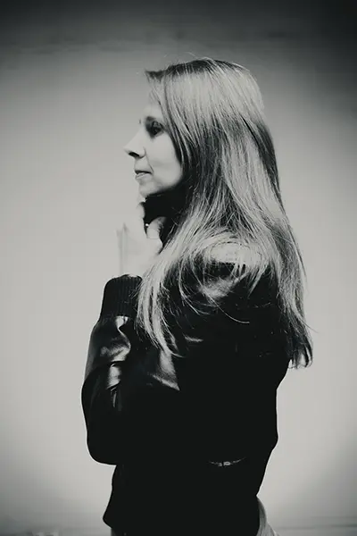 Portrait studio en noir et blanc d’une femme de profil, cheveux longs, veste en cuir, pose élégante sur fond clair, photographe portrait à Bordeaux.