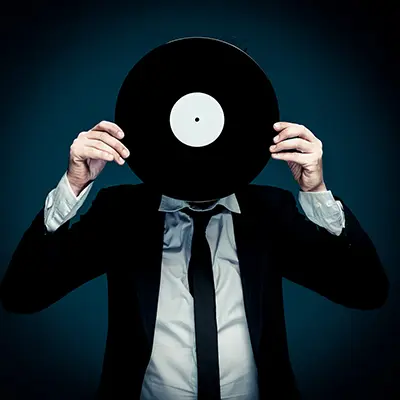 Portrait studio créatif d’un homme en costume et cravate sur fond bleu, tenant un disque vinyle devant le visage, lumière contrôlée — photographe portrait Bordeaux Paris.