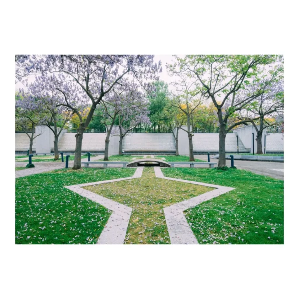 Vue symétrique d'un jardin urbain au Parc de la Villette avec allées géométriques, arbres en fleurs et structures minérales en arrière-plan.