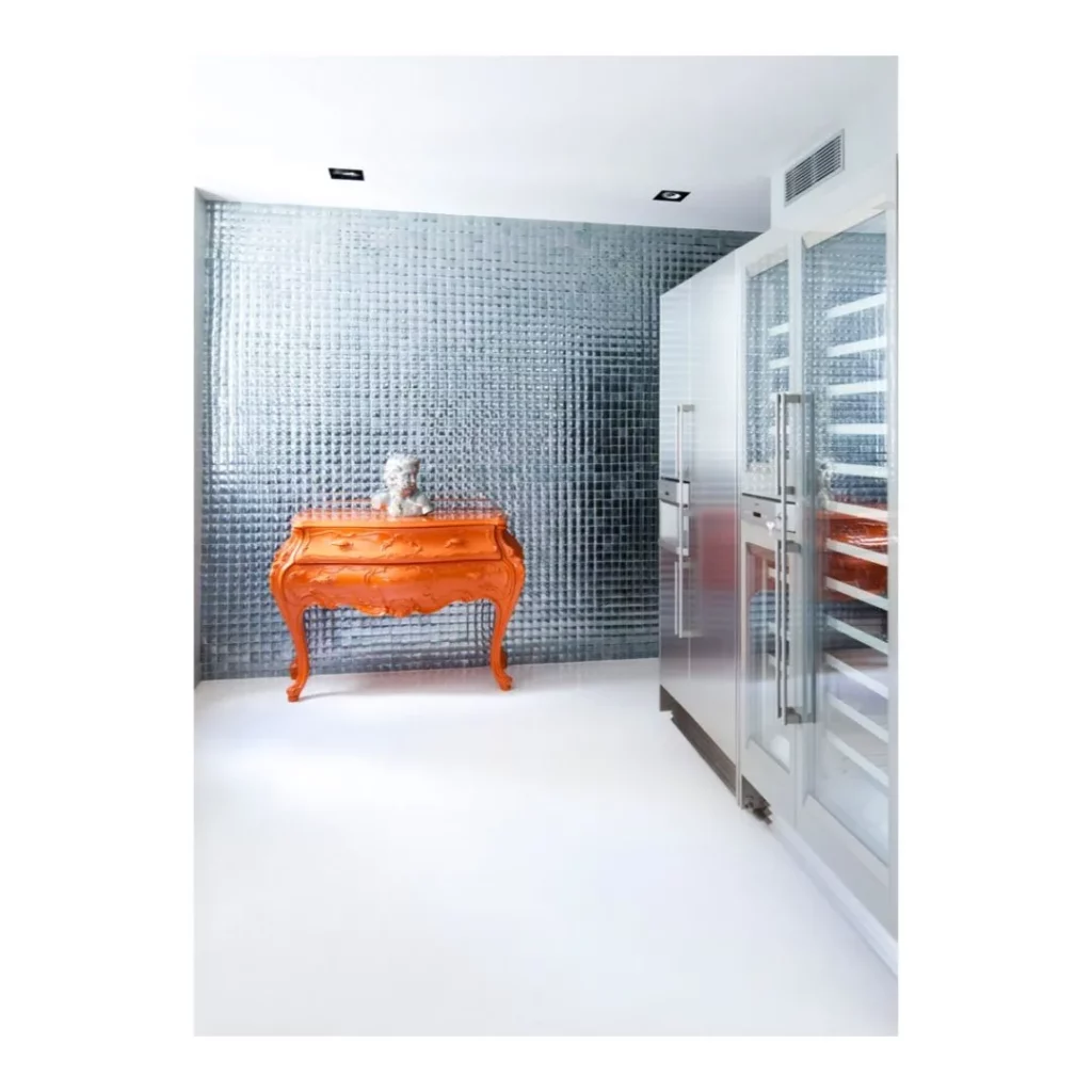 Aménagement intérieur design d'une cuisine moderne comprenant des électroménagers inox intégraux, un mur réfléchissant et un meuble classique orange vif.