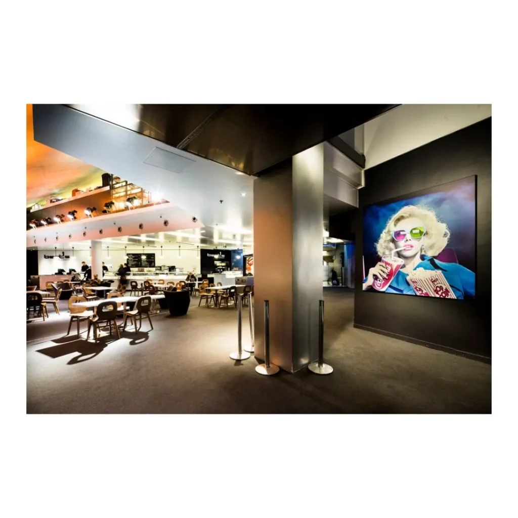 Aménagement intérieur d'un cinéma comprenant un espace café-restaurant et un portrait géant pop art rétroéclairé.