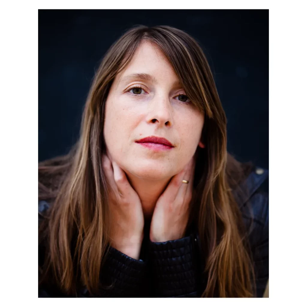 Gros plan d'une femme au regard intense avec les mains sous le menton, portant un blouson en cuir, exercice de portrait lors d'un stage photo à Dieulefit.