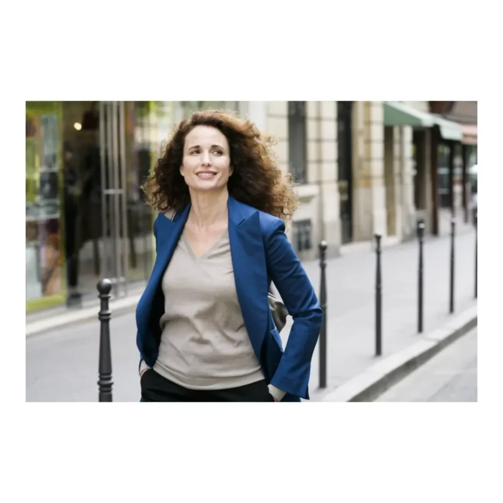 Portrait de style reportage corporate lors d'un making of, montrant une femme d'affaires aux cheveux bouclés marchant dans une rue urbaine avec une veste bleue.