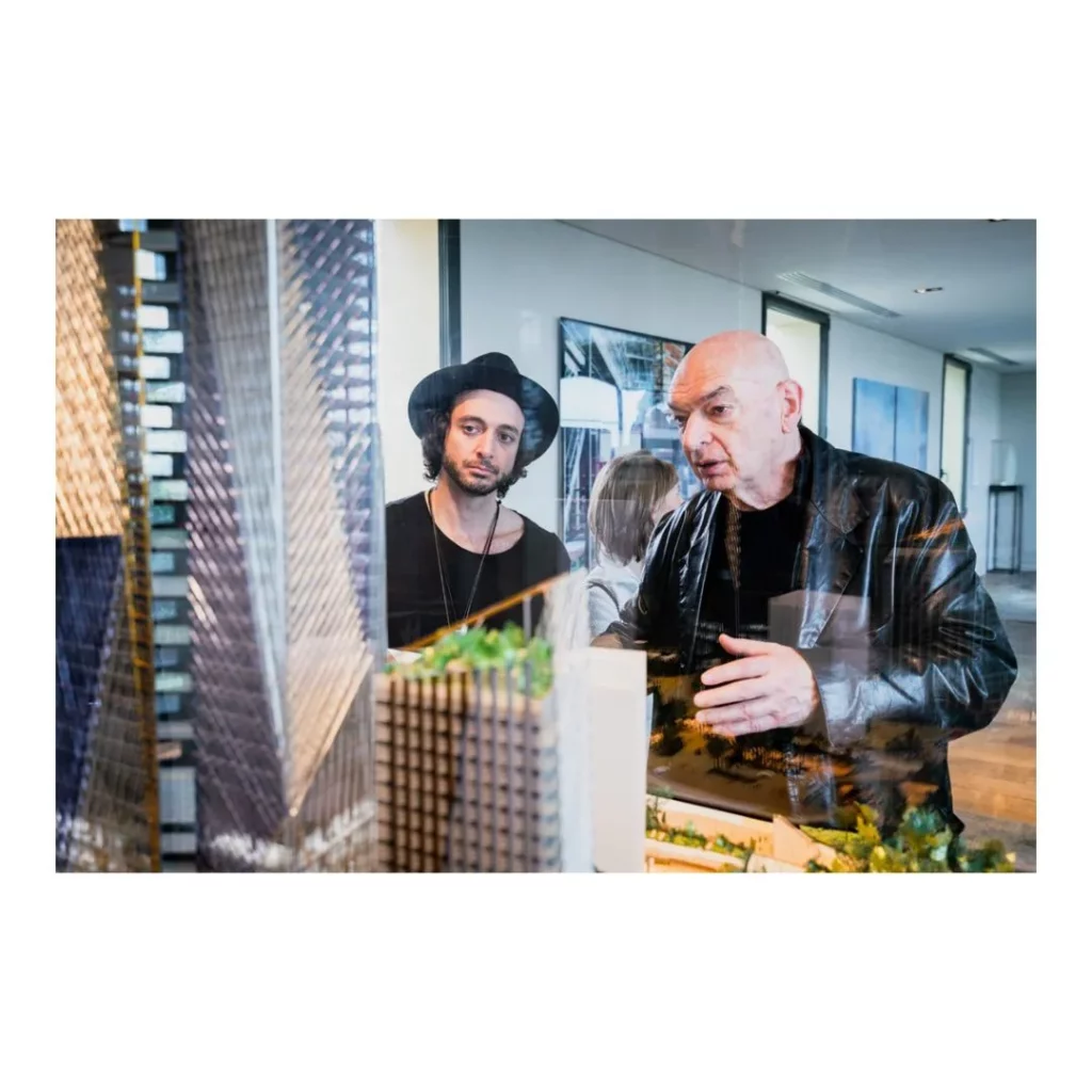 L'architecte Jean Nouvel expliquant un projet architectural devant une maquette détaillée lors d'un making of, dans un cabinet d'architecture.