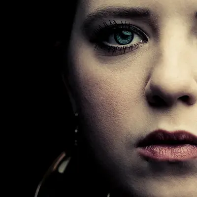 Gros plan macro de portrait beauty montrant le demi-visage d'une femme à l'œil bleu sur fond noir.