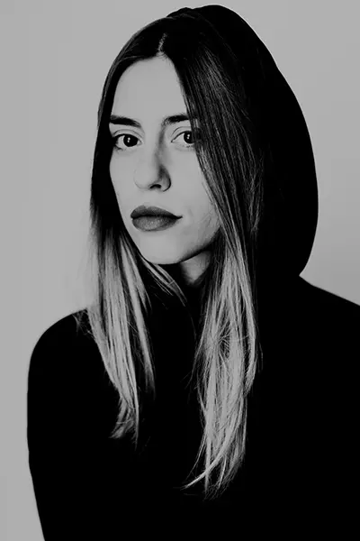 Portrait éditorial en noir et blanc d'une jeune femme portant un haut noir à capuche.