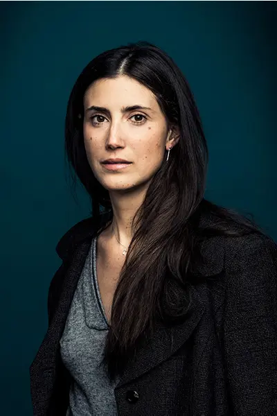 Portrait studio en couleur d'une femme aux cheveux bruns longs en veste sombre sur fond bleu.