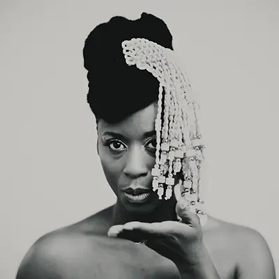 Portrait créatif en noir et blanc d'une femme arborant une coiffe de perles sur fond clair.