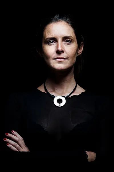 Portrait studio en éclairage dramatique sur fond noir d'une femme portant un pendentif circulaire argenté.