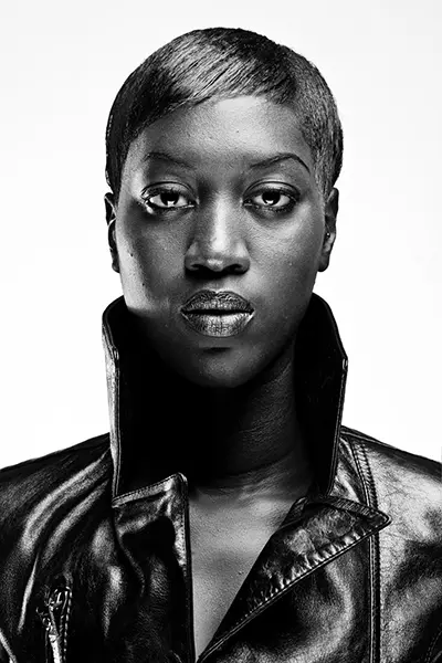 Portrait studio en noir et blanc high key d'une femme aux cheveux courts portant une veste en cuir au col relevé sur fond blanc.