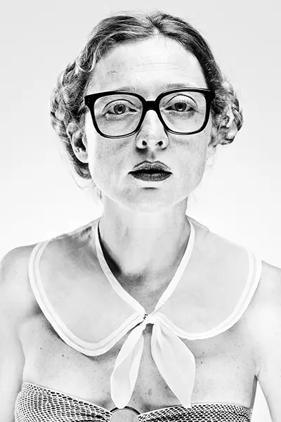 visuellement) Portrait studio en noir et blanc high key d'une femme à lunettes noires et col marin noué sur fond blanc.