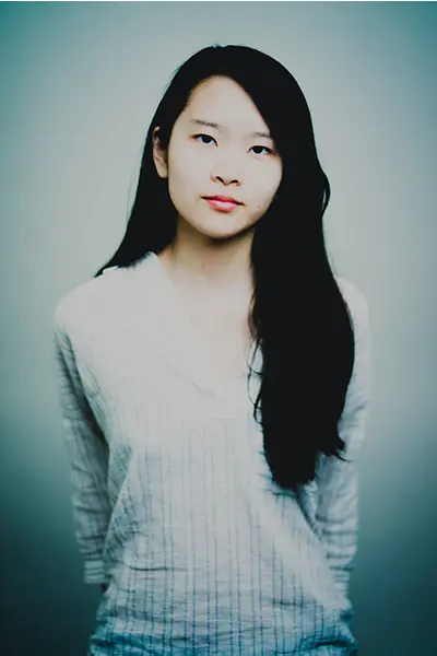 Portrait studio simple et naturel d'une jeune femme aux cheveux longs portant une blouse rayée claire sur fond gris.