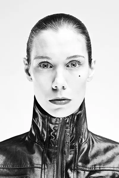 Portrait studio en noir et blanc high key d'une femme en veste de cuir à col zippé, regard direct sur fond blanc. Portrait graphique de femme en noir et blanc - Nicolas Louis