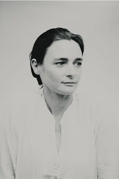 Portrait studio en trois-quarts noir et blanc d'une femme au regard détourné en chemise claire.