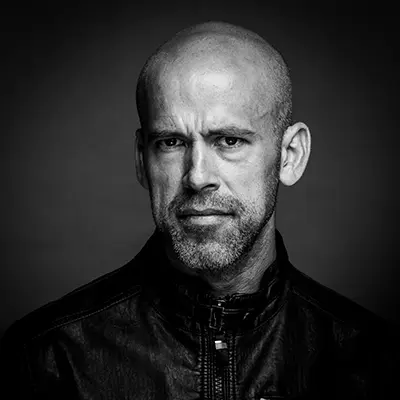 Portrait studio en noir et blanc d'un homme chauve à barbe courte portant une veste en cuir.